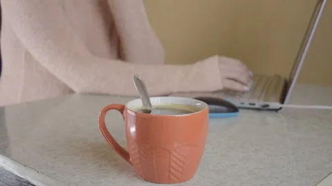 The girl is working at the computer. He drinks hot coffee from an orange mug. 스톡 동영상 95254351