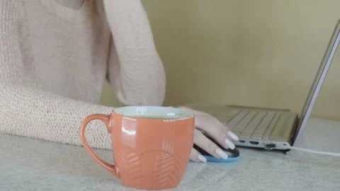 The girl is working at the computer. He drinks hot coffee from an orange mug. Stockbeeldmateriaal 95254361