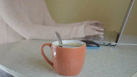 The girl is working at the computer. He drinks hot coffee from an orange mug. Vídeo Stock 95254394