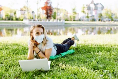 Girl working at the computer lying on the grass in a protective medical mask  Stock Photos