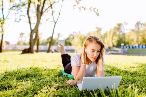 Girl working at the computer lying on the grass in a park. Freelance, distanc Stock-Fotos