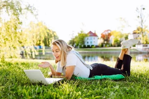 Girl working at the computer lying on the grass in a park. Freelance, distanc Stock Photos