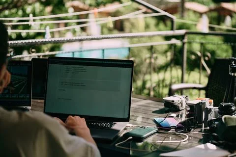A girl working on the table on the terrace. Many laptops and other staff. Back Stock Photos