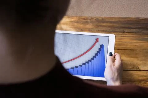 The girl working with a tablet computer. The graph rises. Table, wooden, back Stock Photos