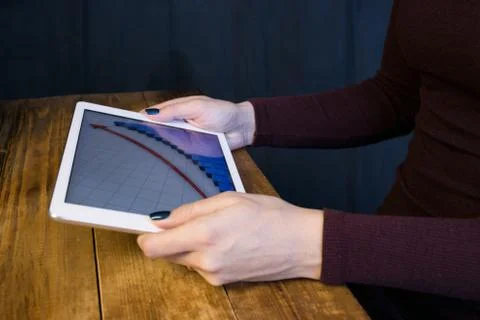 The girl working with a tablet computer. The graph rises. Table, wooden, back Stock Photos