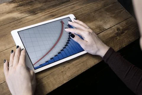 The girl working with a tablet computer. The graph rises. Table, wooden, back Stock Photos