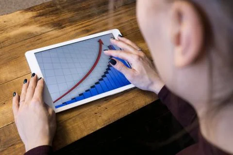 The girl working with a tablet computer. The graph rises. Table, wooden, back Stock Photos