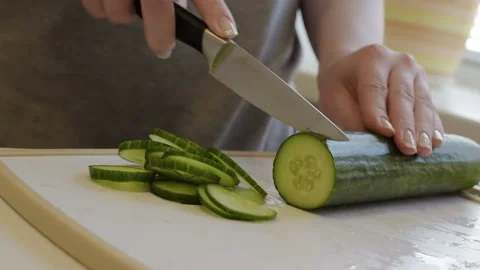 The girl works in the kitchen, cuts cucumbers on a white board. Stock Footage 106930513