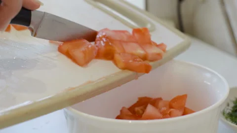 The girl works in the kitchen, throws sliced tomatoes in a bowl. Stock Footage 106930122