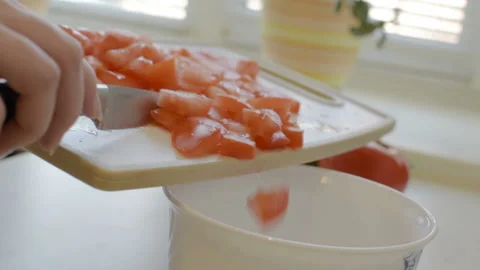 The girl works in the kitchen, throws sliced tomatoes in a bowl. Vídeo Stock 106930222