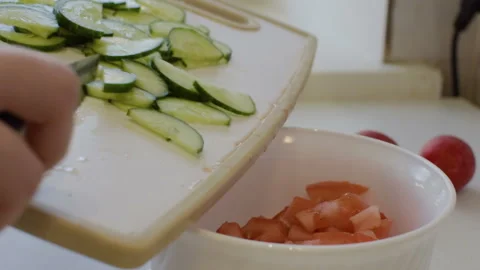 The girl works in the kitchen, throws sliced cucumbers in a bowl. Vídeo Stock 106930570