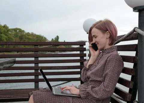 Girl works for a laptop. at the table on the street against the background of Photos