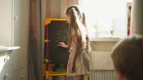Girl writes math problems on blackboard teaching brother Stock Footage 248022708