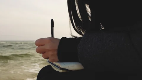 The girl writes in a notebook with a pen on the background of the sea Stock Footage 103053111