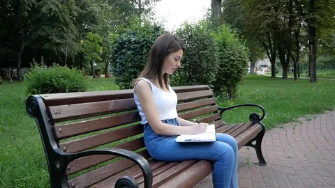 Girl writes in a notebook, sitting on a bench in the Park Video stock 100596293