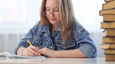The girl writes in a notebook at a white table with books. Video stock 244878037
