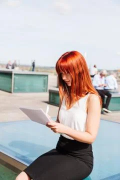 Girl writes something on forms sitting on street Foto stock