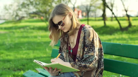 Girl writing something in notebook while sitting in the park Stock-Footage 62439142
