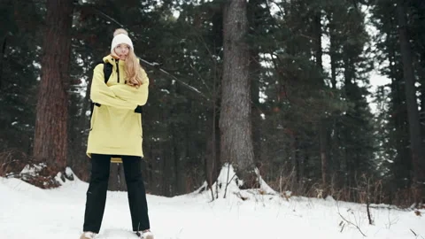 A girl in a yellow jacket crouches in the forest in winter to keep warm Stock Footage 144696341