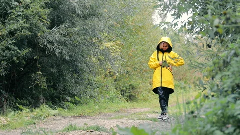 A girl in a yellow raincoat stands in the forest on the road and uses a mobile Stock Footage 252213853