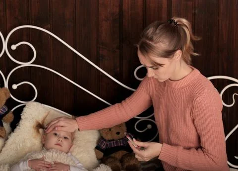 Girl, a young mother measures the temperature of her child. looks at the ther Photos