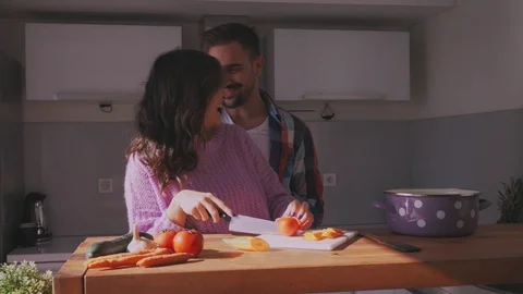 Girlfriend cuts tomato in kitchen and boyfriend is kissing her Stock Footage 97646293