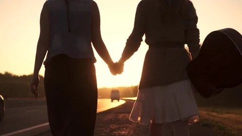 Girlfriend go on the road in the rays of the rising sun and holding hands Stock Footage 77236385