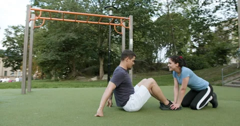 Girlfriend helping boyfriend do situps at the outdoor gym. Stock Footage 130219992