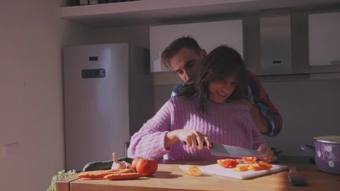 Girlfriend making salad in kitchen and boyfriend is kissing her Stock Footage 97645969