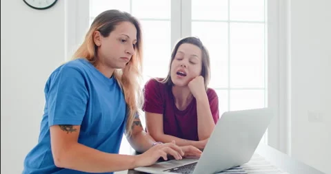 Girlfriends sitting together in the kitchen with notebook Stockbeeldmateriaal 134478801