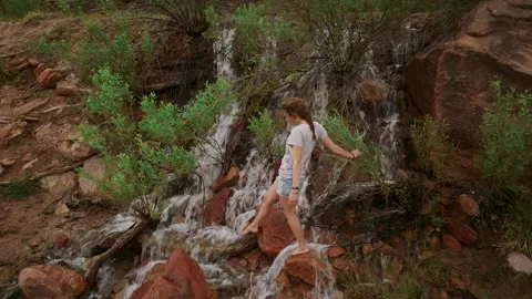 Girls balanced on rocks while crossing a stream in a natural setting Stock Footage 321428341