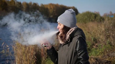 Girls elegantly smokes an e-cigarette and blows smoke in the park portrait Stock-Footage 72706808