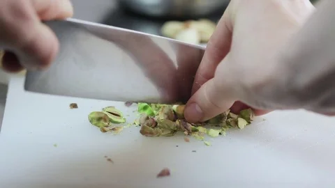A girls hand cutting & chopping fresh pistachios with a knife on a board Stock Footage