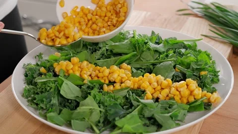 The girl's hand spoons canned corn onto the lettuce leaves. Stock Footage 253994553