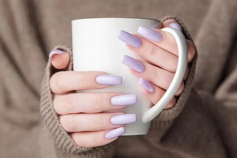 Girl's hands with delicate purple manicure holding a cup of tea. Stock Photos