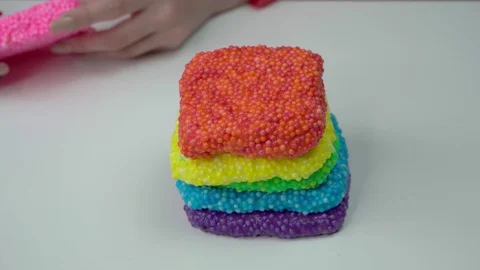 Girl's hands make a square slice of different color slimes with foam balls Stock Footage 127596542