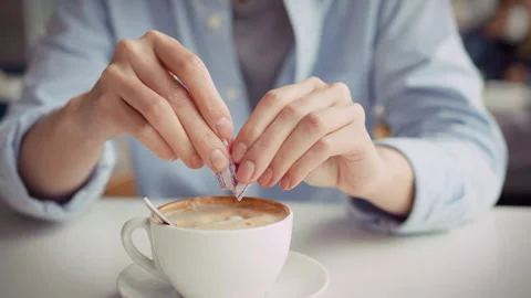 Girls hands sprinkle sugar from packet into a fresh cappuccino at a daytime Stock Footage 342240508