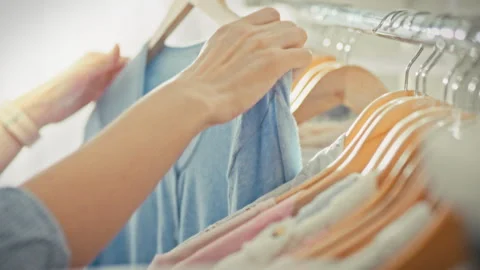 A girls hands thoughtfully select garments from wooden hangers on a metal ra Stock Footage 345526862