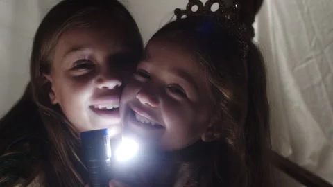 Girls having fun playing flashlight games under a sheet in the living room Stock Footage 320030395