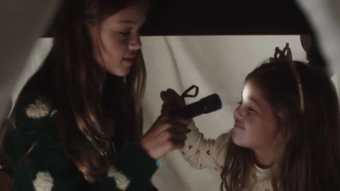 Girls having fun playing with flashlights inside a cozy fort at night Stock Footage 320030859