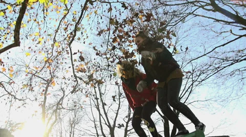 Girls shot from low angle throw leaves and jump from a bench Stock Footage 33734983