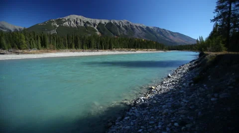 GLACIAL BLUE RIVER FLOWS BY WITH MOUNTAIN IN THE BACKGROUND - 1 Stock Footage 59072442