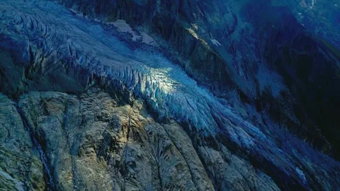 Glacial ice flow cascading down steep rocky mountain face under dramatic natural Stock Footage 343696103