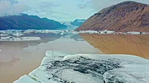 Glacial lagoon drone shot flying over melting icebergs with mountain reflections Stock Footage 343696290