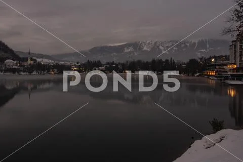 Glacial lake with town, forest and snowy mountains Stock Photos