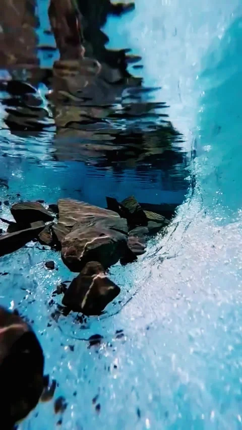Glacial meltwater flow reveals underwater rocks and ice formations on sunny.. Stock Footage 333607071