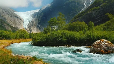 Glacial river flows through a lush green valley with snow-capped mountains .. Vídeos de archivo 334830711