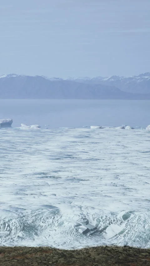 Glacier ice meets ocean waters with mountains in background under blue sky Stock Footage 343187638