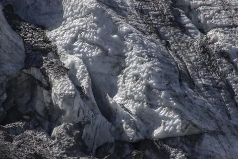 Glacier ice texture featuring white snow and dark rocks Stock Photos