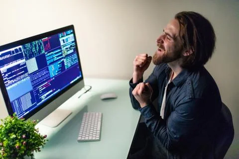 Glad bearded man programer working on computer with win gesture 스톡 사진